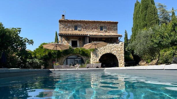 A pool with clear water, a stone building with a tiled roof, and umbrellas. - 18th CENTURY STONE BASTIDE in UZES (La Bastide-d'Engras)