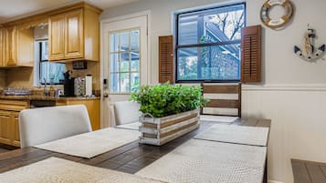 Un área de comedor con una mesa de madera, dos sillas, un mantel tejido y una maceta con plantas verdes.