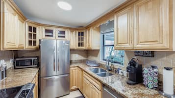 Una cocina moderna con armarios de madera, electrodomésticos de acero inoxidable, encimeras de granito y una estación para café.