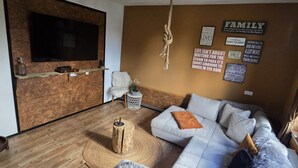 Un salon moderne doté d’un grand téléviseur à écran plat fixé sur un mur en bois, d’un canapé agrémenté de nombreux coussins, d’un luminaire suspendu et d’œuvres d’art murales inspirantes.