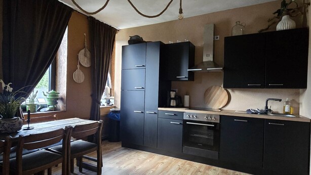 Une cuisine moderne avec des meubles de rangement sombres, une table à manger en bois et un ventilateur de plafond.