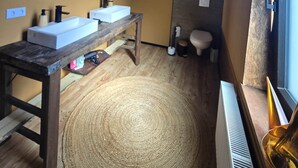 Une salle de bain avec deux lavabos, une table en bois, un tapis rond et une fenêtre donnant sur un beau paysage.