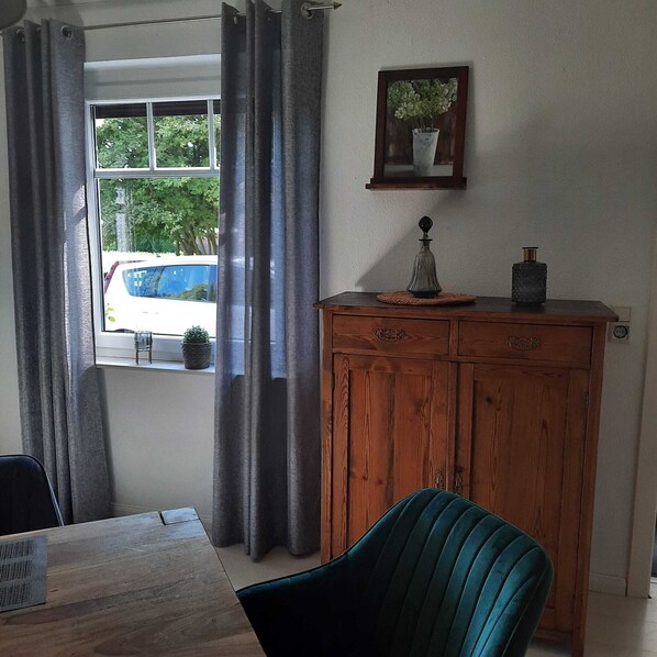 Una habitación con un armario de madera, una mesa, una silla y una ventana con cortinas.