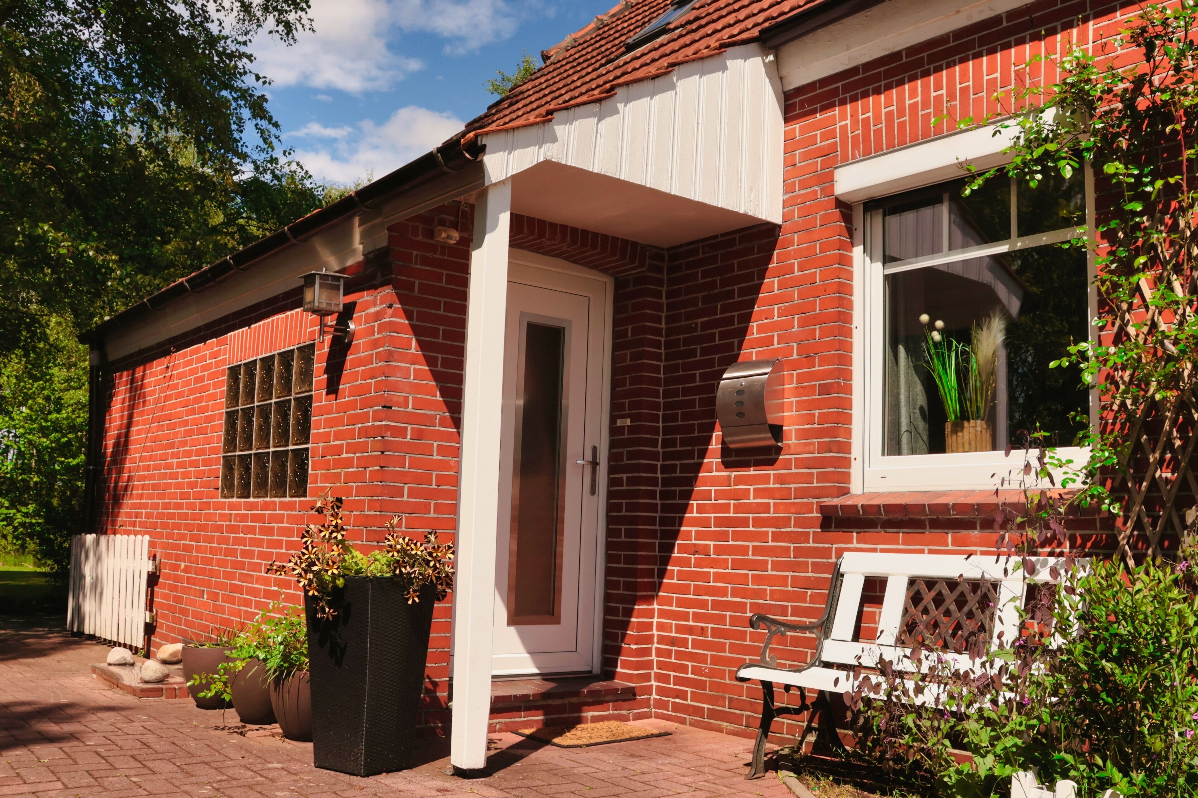 A red brick building with a white door, a window with a view, and a bench outside.