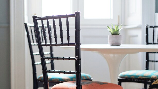 Un área de comedor con una silla negra con asiento y respaldo acolchados, una mesa blanca y una planta en maceta sobre la mesa.