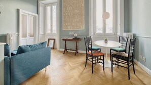 A room with a blue sofa, a round dining table with chairs, and large windows. - Ferrucci 14 by Wynwood House (Milan)