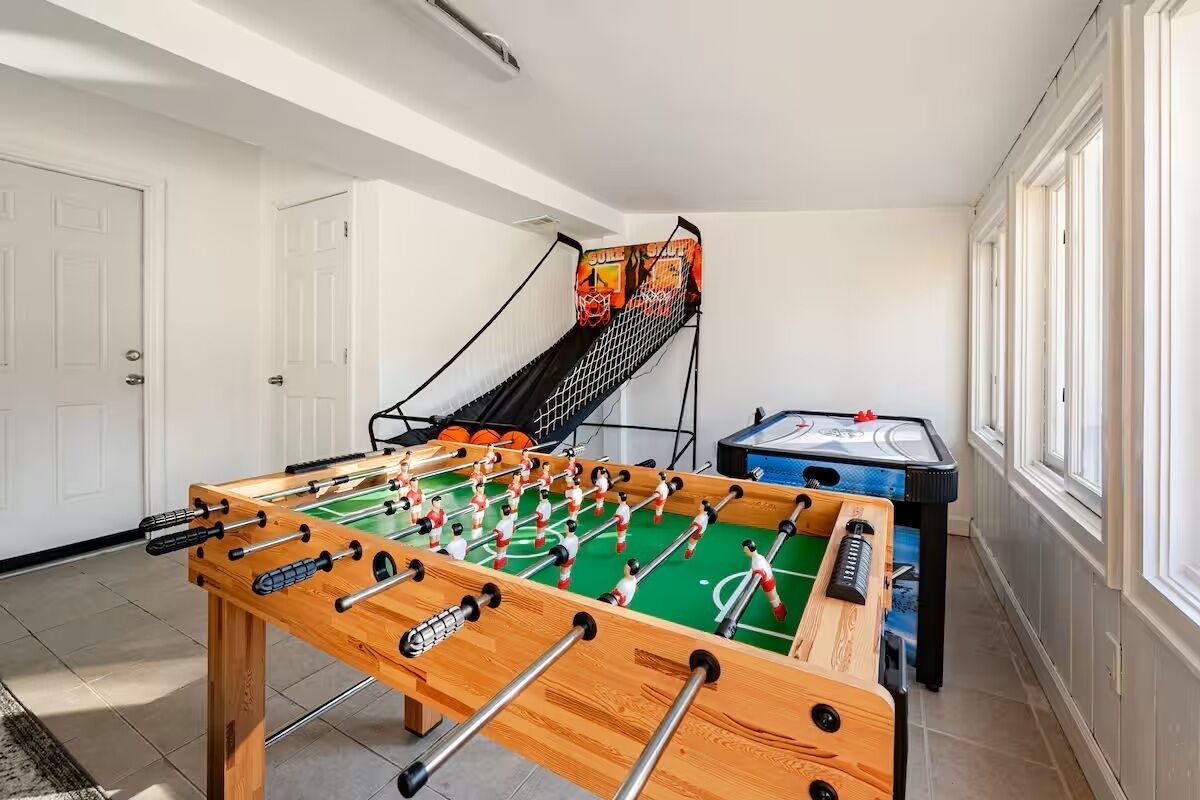 A room with a foosball table, a pool table, and a staircase with a basketball court mural.