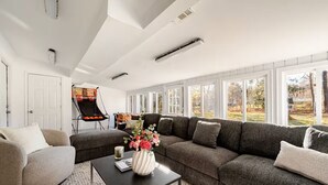 Un salon moderne avec un canapé d’angle, une table basse et une petite table d’appoint. Une fenêtre offre une vue sur l’extérieur.
