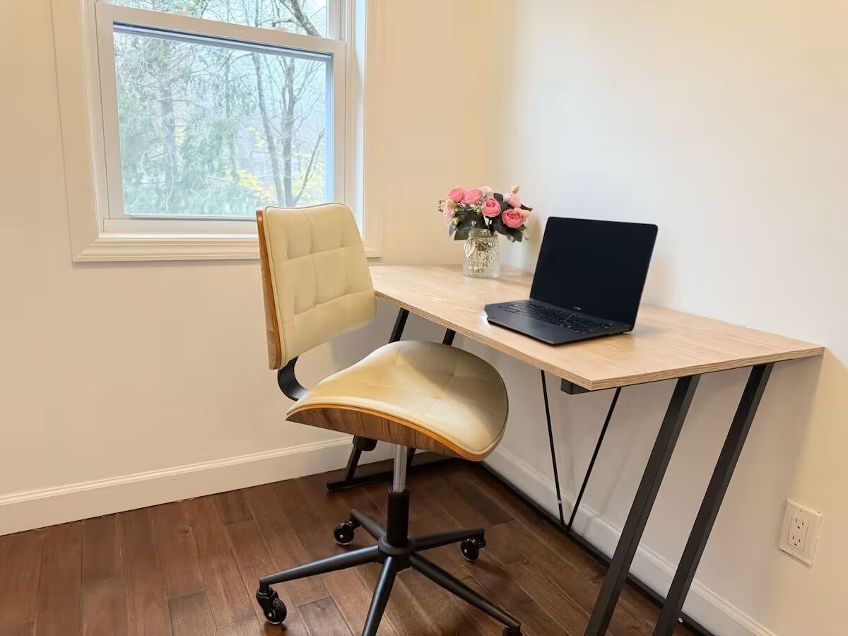 A workspace with a desk, chair, laptop, and a vase with flowers.