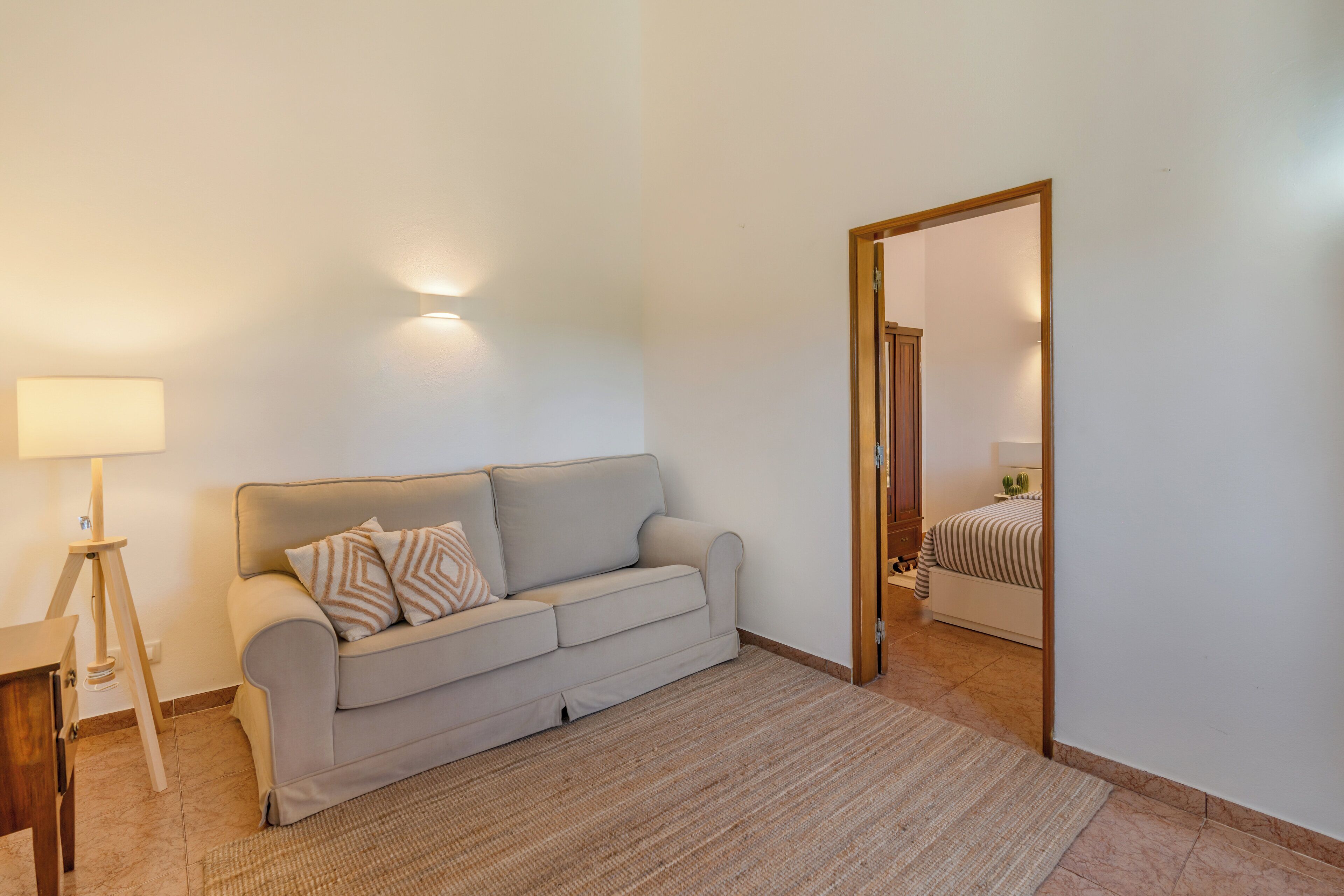 A living room with a sofa, a lamp, and a mirror reflecting a bed.