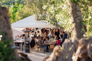 An outdoor dining area with tables and chairs under a large tent, surrounded by trees. - Quinta dos Capinhas (Lagoa)
