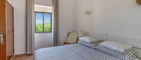 Une chambre d’hôtel avec un lit, une chaise, une fenêtre avec des rideaux et une lampe fixée au mur.