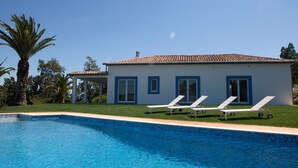 A modern house with a swimming pool, white walls, and blue trim. There are three lounge chairs by the pool.