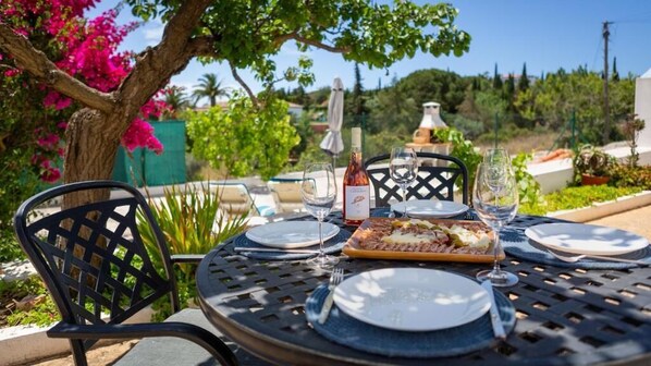 A round table set outdoors with a bottle of wine, glasses, and a plate of food. - Quinta dos Capinhas (Lagoa)