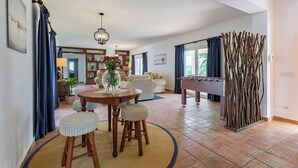 A spacious living area with a round wooden table, two stools, a foosball table, and a decorative plant centerpiece.