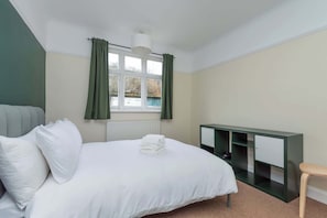 A bedroom with a bed, a window with curtains, a radiator, a green cabinet, and a wooden stool. - Spacious 2BDR with Dedicated Work Area (Greater London)