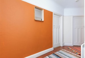 A hallway with an orange wall, a mirror, white doors, and a patterned rug. - Spacious 2BDR with Dedicated Work Area (Greater London)