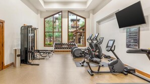 Une salle de sport équipée d’appareils de cardio, d’haltères et d’un téléviseur fixé au mur.