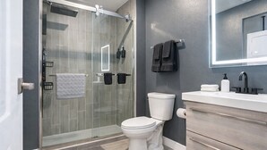 Un baño moderno con cabina de ducha de vidrio, inodoro, lavamanos con espejo y toallero.