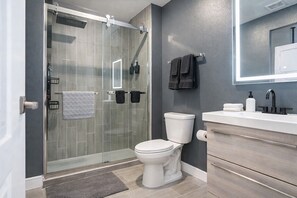 Ein modernes Badezimmer mit Duschkabine aus Glas, Toilette, Waschbecken mit Spiegel und Handtuchhalter.