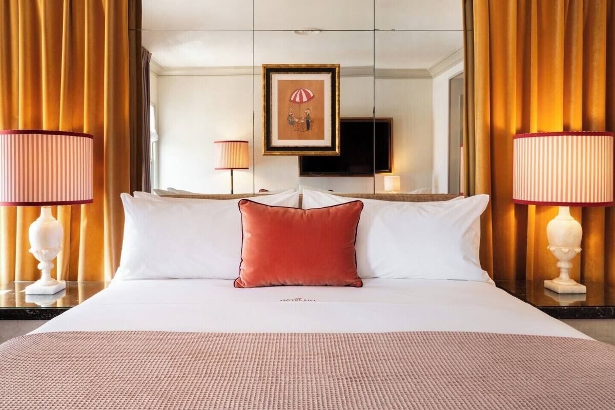 A hotel room with a large bed, two bedside lamps, a framed picture above the bed, and a television on the wall.