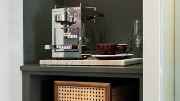 Une machine à café posée sur une étagère, avec un verre et une tasse.
