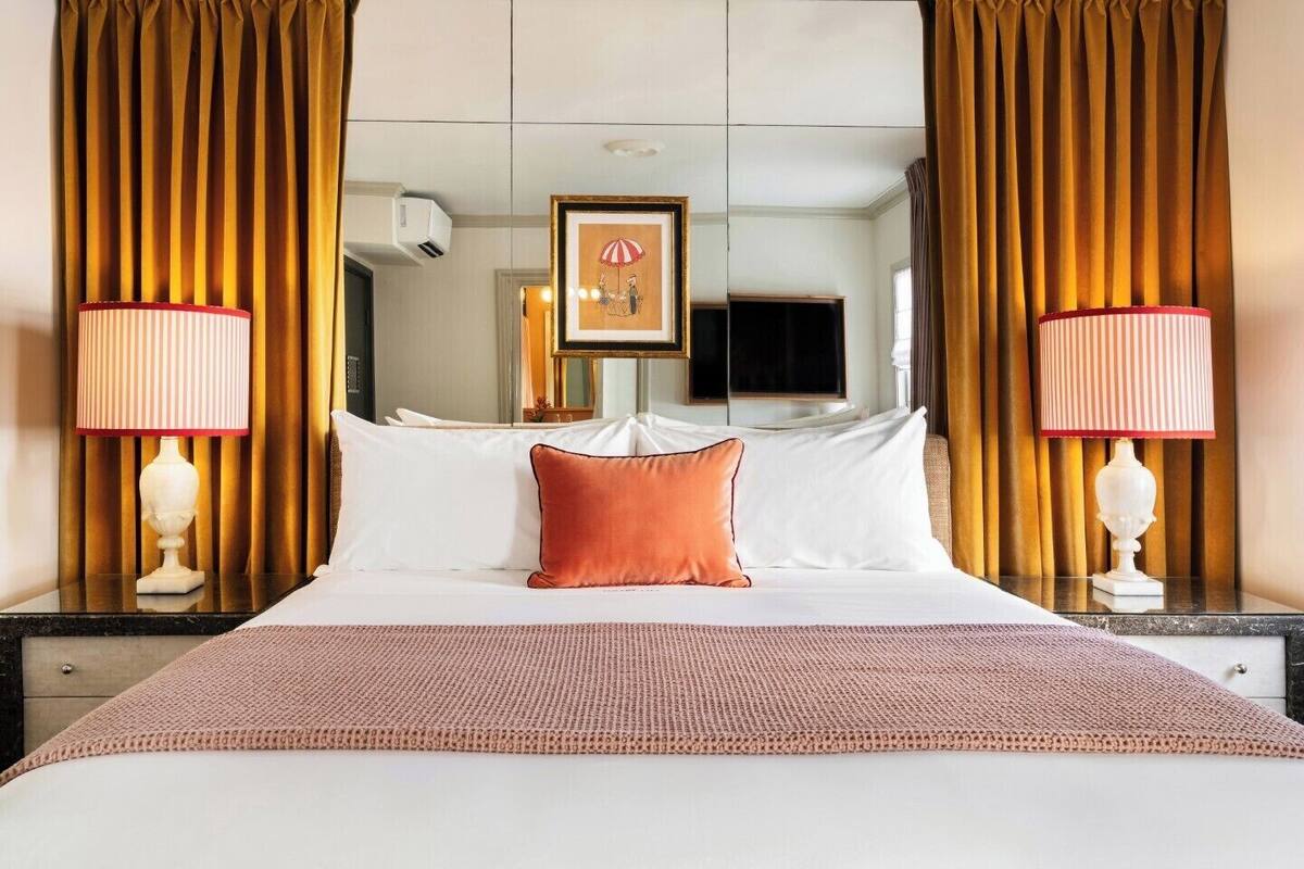 A hotel room with a large bed, two bedside lamps, a framed picture on the wall, and a mirror above the bed.