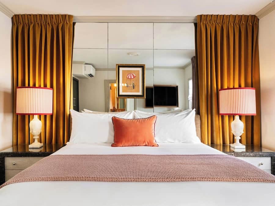 Habitación de hotel con una cama grande, dos lámparas de noche, un cuadro en la pared y un espejo sobre la cama.