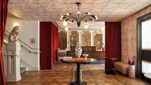 A hotel lobby with a herringbone floor, a grand staircase, a reception desk, and a decorative ceiling. - The Hotel Lili - Beverly Hills (Beverly Hills)
