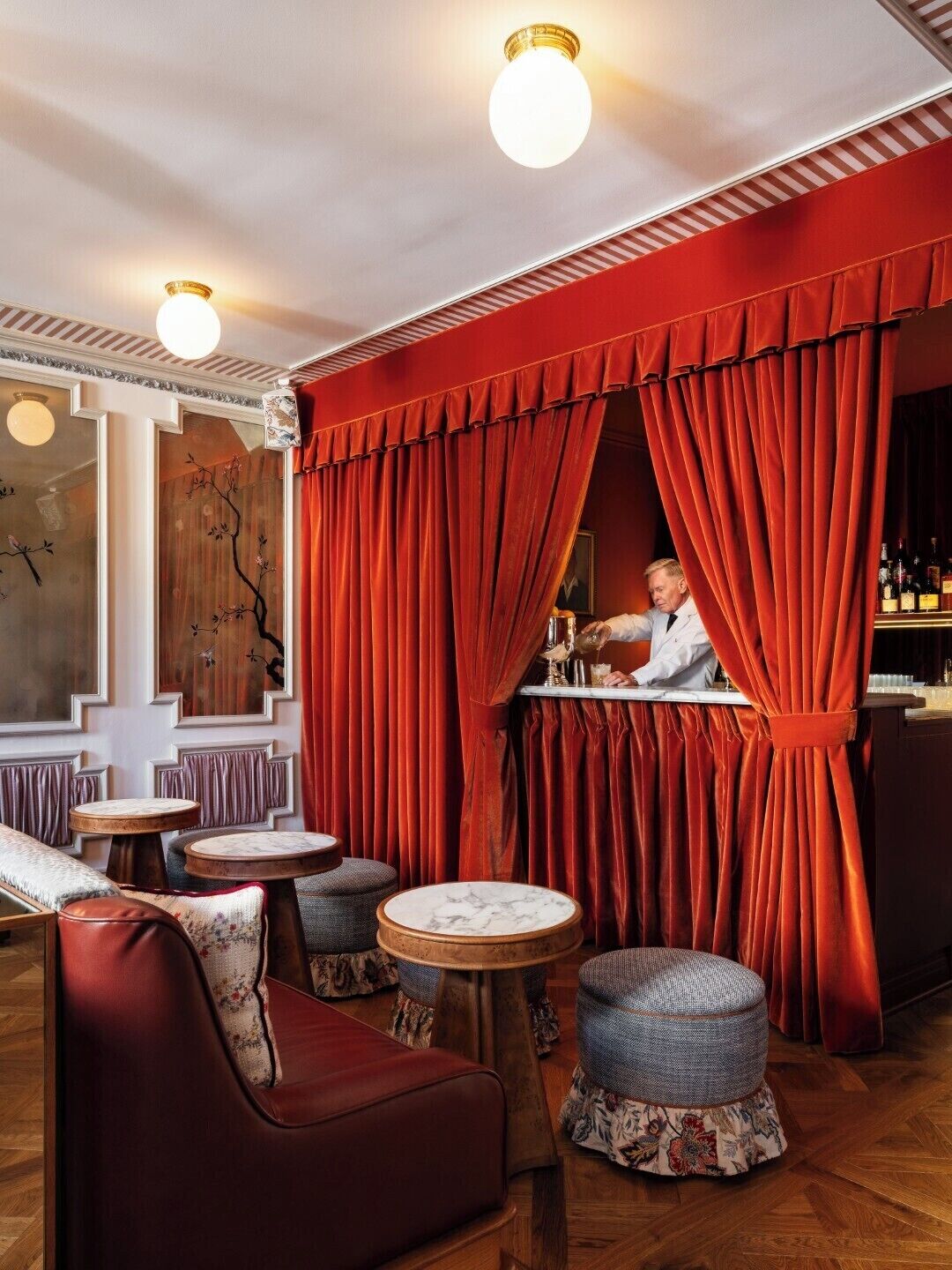 A bar area with red curtains, wooden flooring, and round tables with stools.