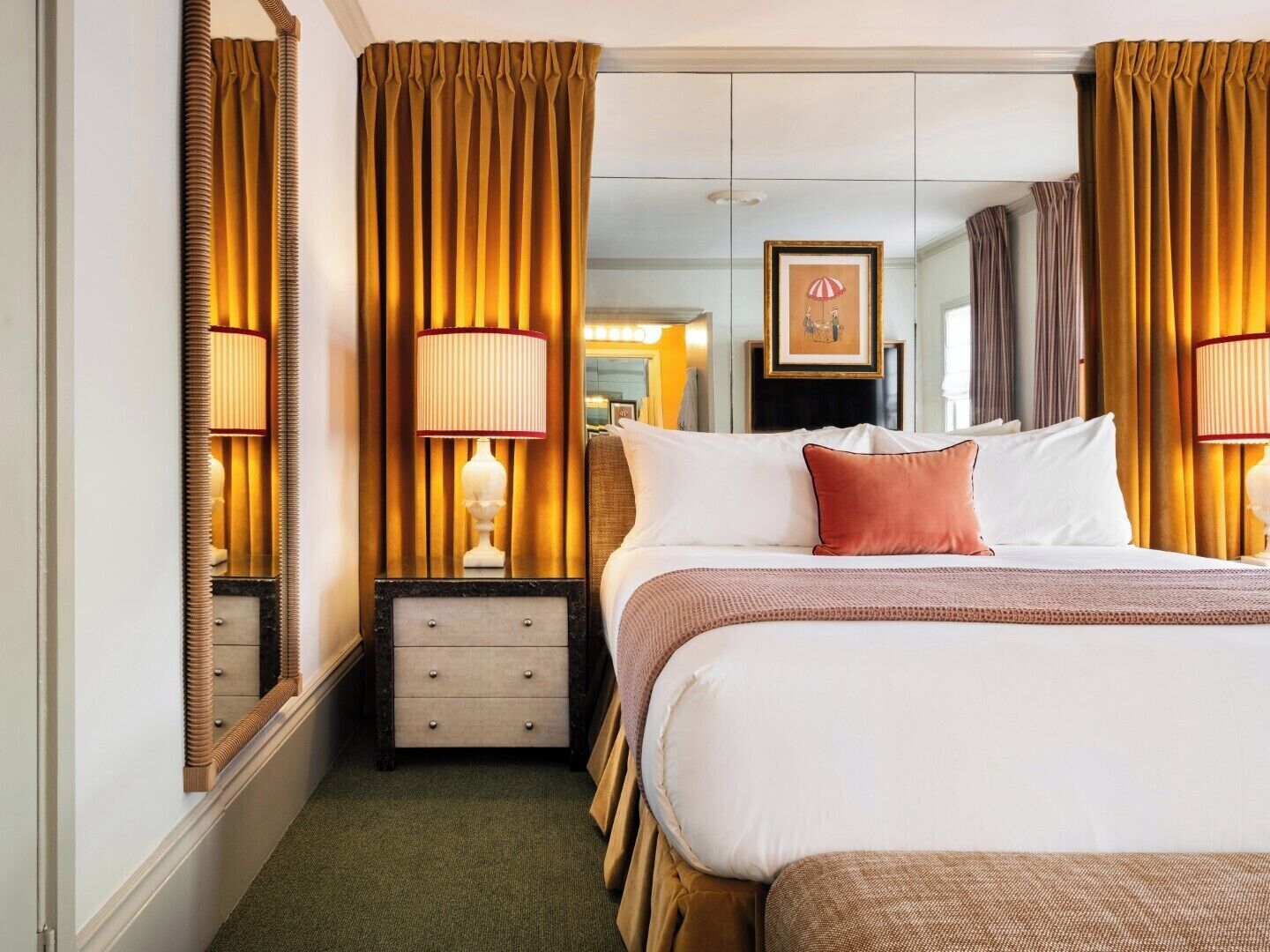 A hotel room with a large bed, two bedside lamps, a dresser, a mirror, and a framed picture on the wall.