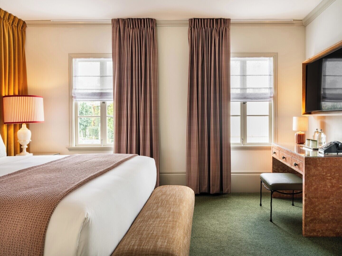A hotel room with a bed, a desk, a chair, two windows, and a television.