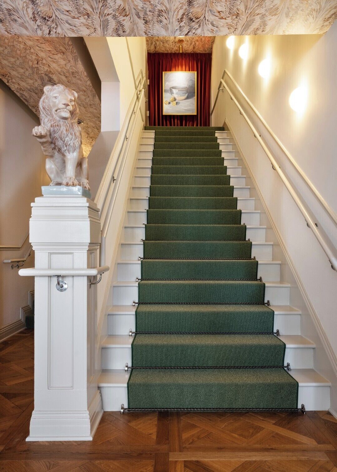 A staircase with green carpeted steps, a white handrail, and a lion statue on the left.