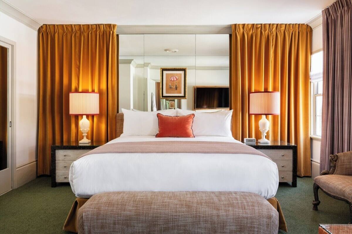 A hotel room with a large bed, two bedside tables, a chair, and a mirror.
