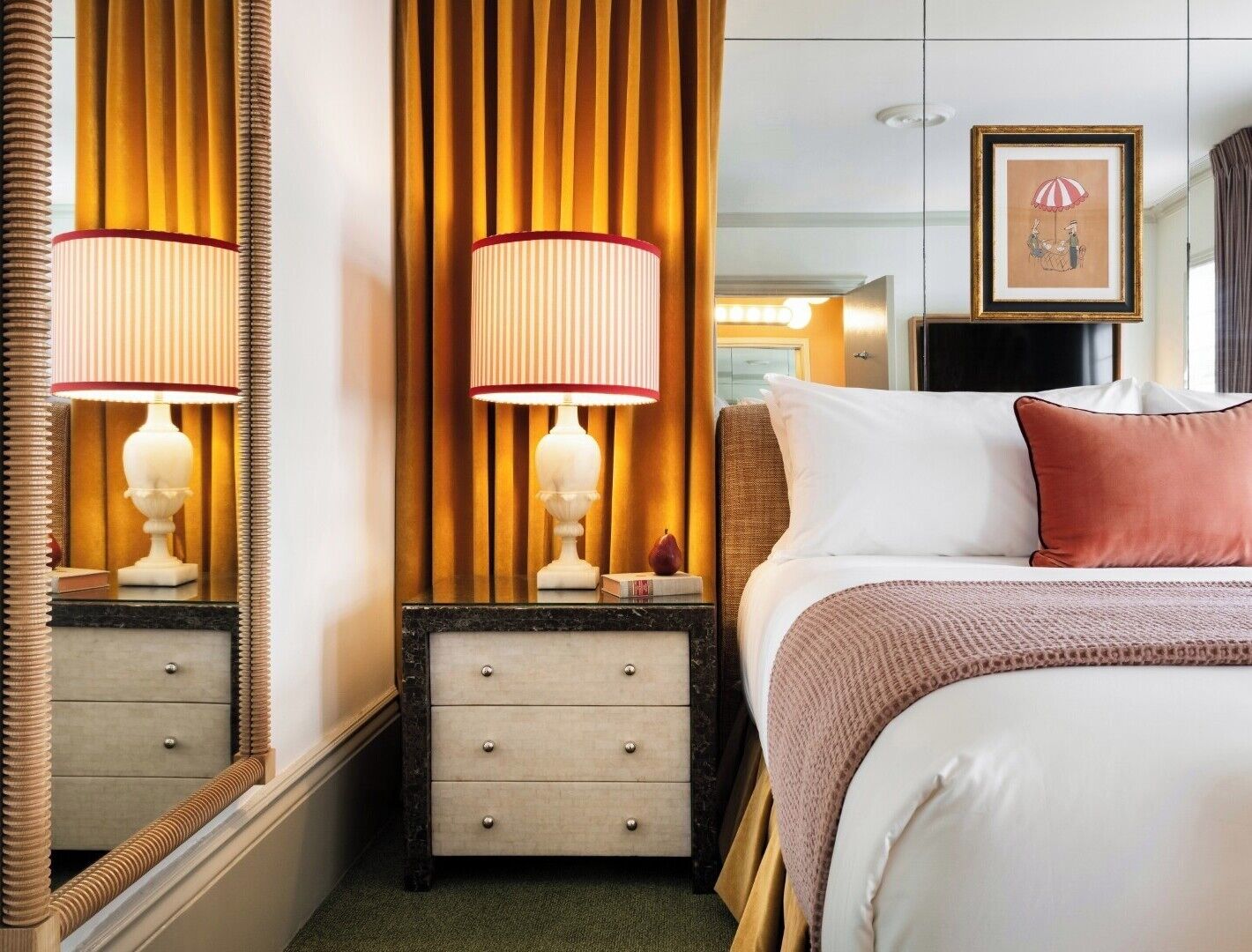 Een hotelkamer met een bed, nachtkastje met lamp, een dressoir, een spiegel en een ingelijste foto aan de muur.