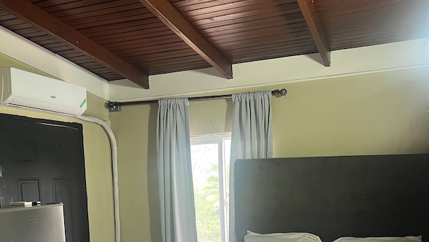 Un dormitori amb llit, finestra amb cortines, una porta i un frigorífic.