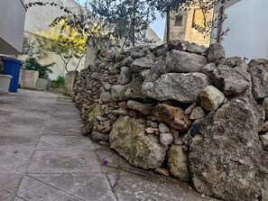 Um muro de pedra, um pátio com azulejos e um edifício ao fundo.