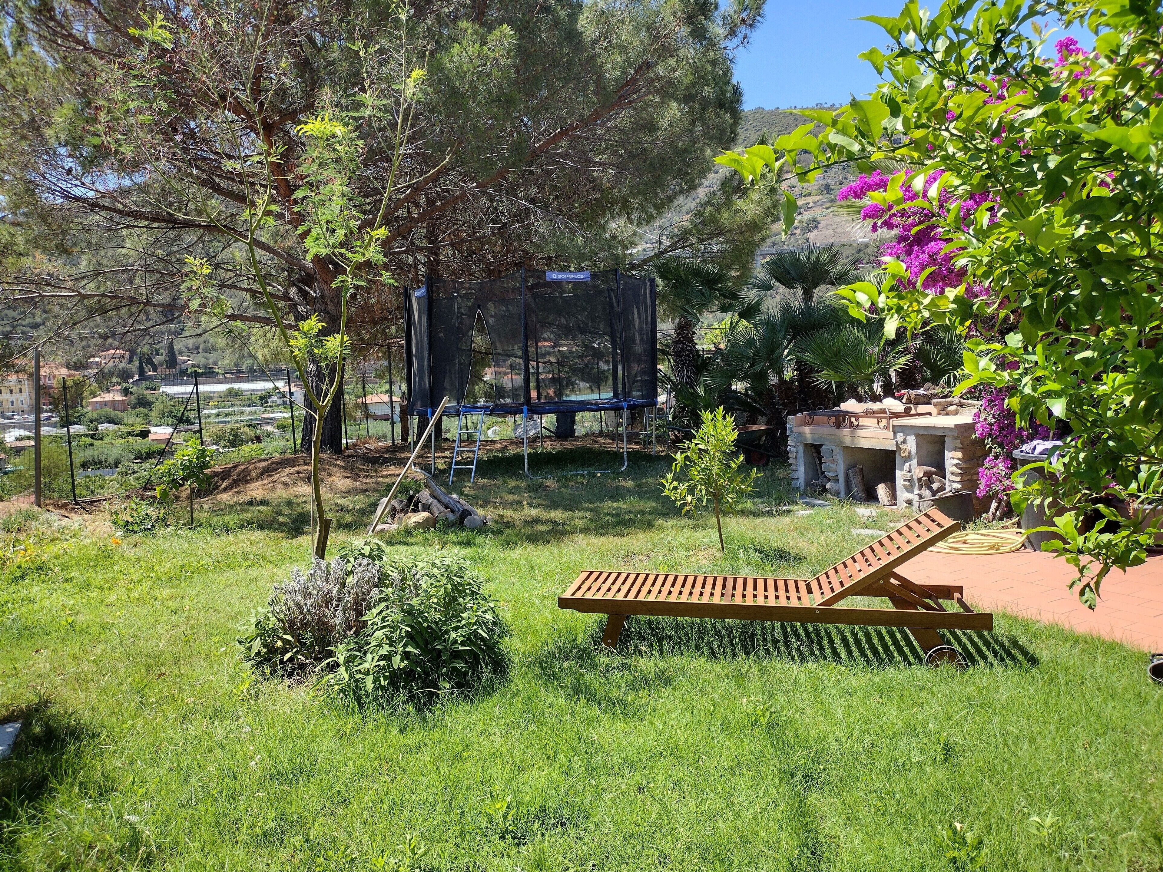 Un jardin avec un banc en bois, un trampoline et une structure en pierre.