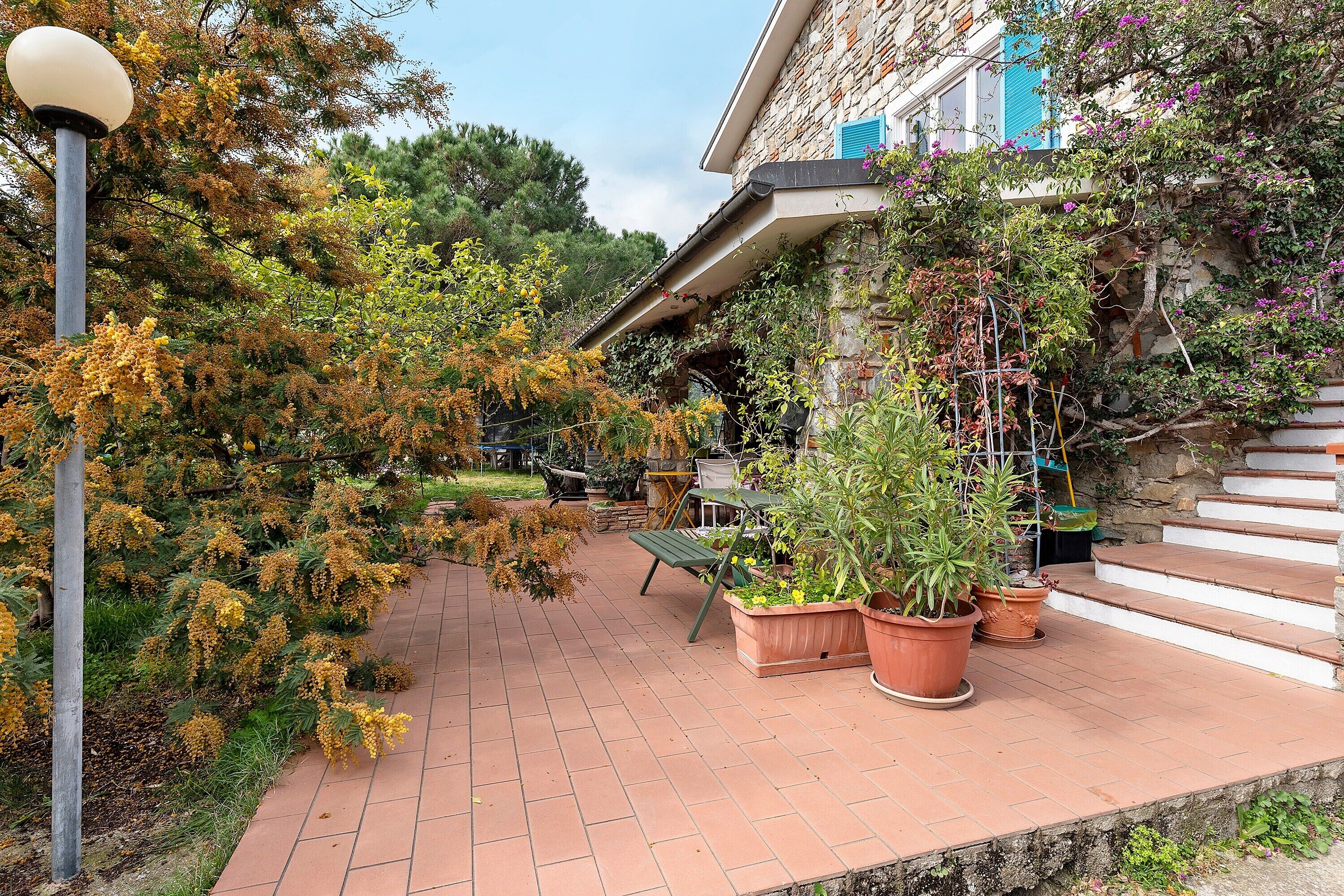 A courtyard with a stone building, potted plants, a bench, and a lamp post.