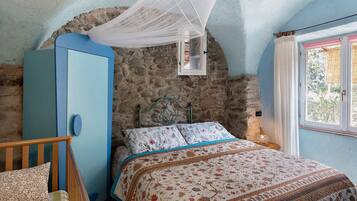 Een slaapkamer met een stenen muur, een blauwe garderobe, een bed met bloemenbeddengoed en een hemelbed.