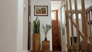Una scala conduce a una stanza con ringhiera in legno, un quadro appeso al muro e due grandi piante in vaso.