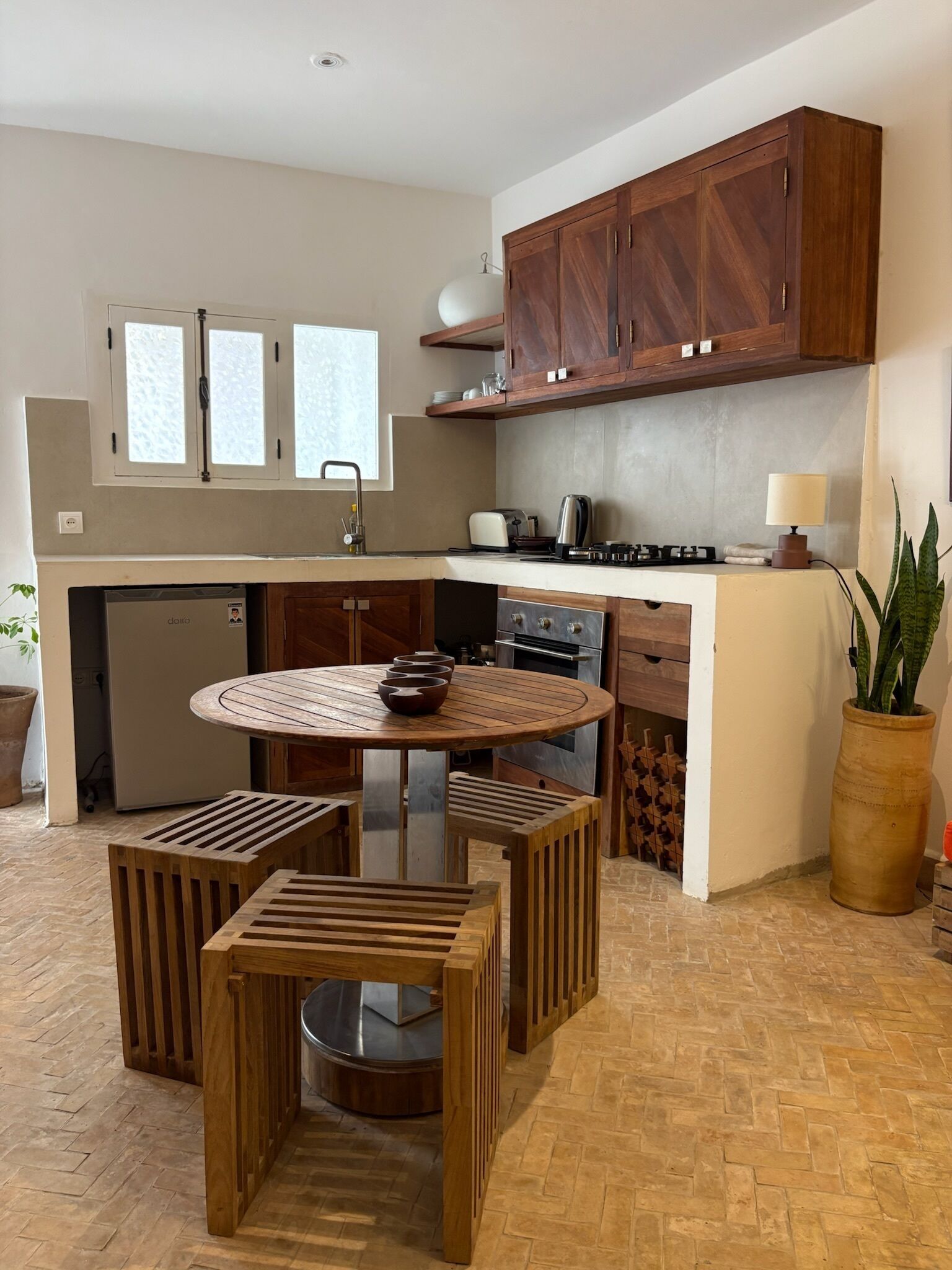 Una cocina compacta con armarios de madera, horno empotrado, mesa redonda y una planta en maceta.