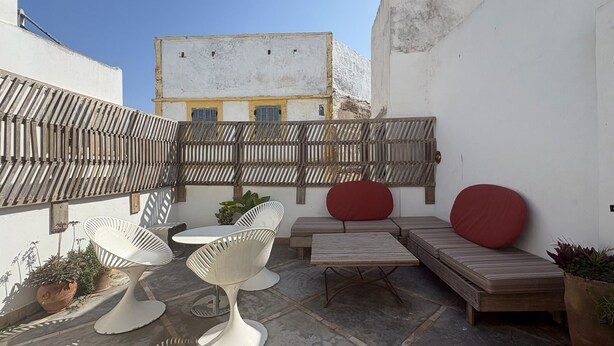 Una terrazza sul tetto con un muro bianco, una recinzione di legno e zone relax con tavolo e sedie.