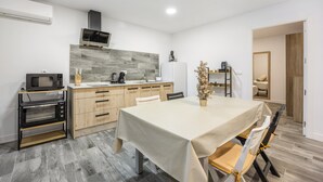 Ett modernt kök med mikrovågsugn, ugn och kaffebryggare, ett matbord med stolar och ett träskåp.