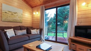 A cozy cabin interior with a sofa, a coffee table, a TV, and a sliding glass door leading to a patio.