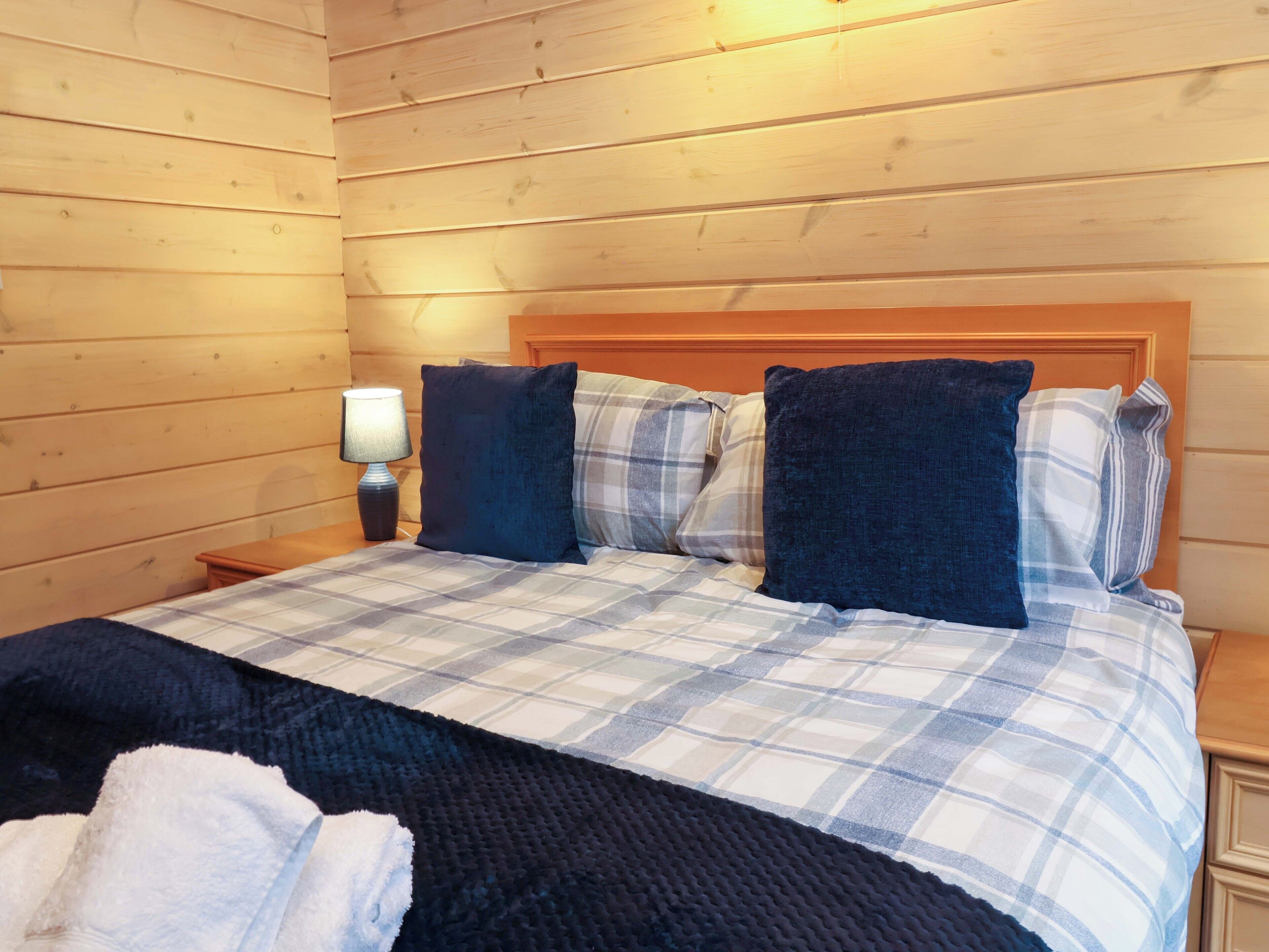 Een kamer met houten lambrisering, een bed, een nachtkastje en een lamp.