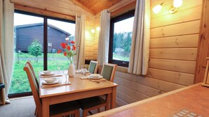 A wooden dining room with a table set for four, large windows with curtains, and a view of a house and greenery outside.