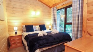 A cozy wooden cabin bedroom with a bed, nightstands, and a window with curtains.