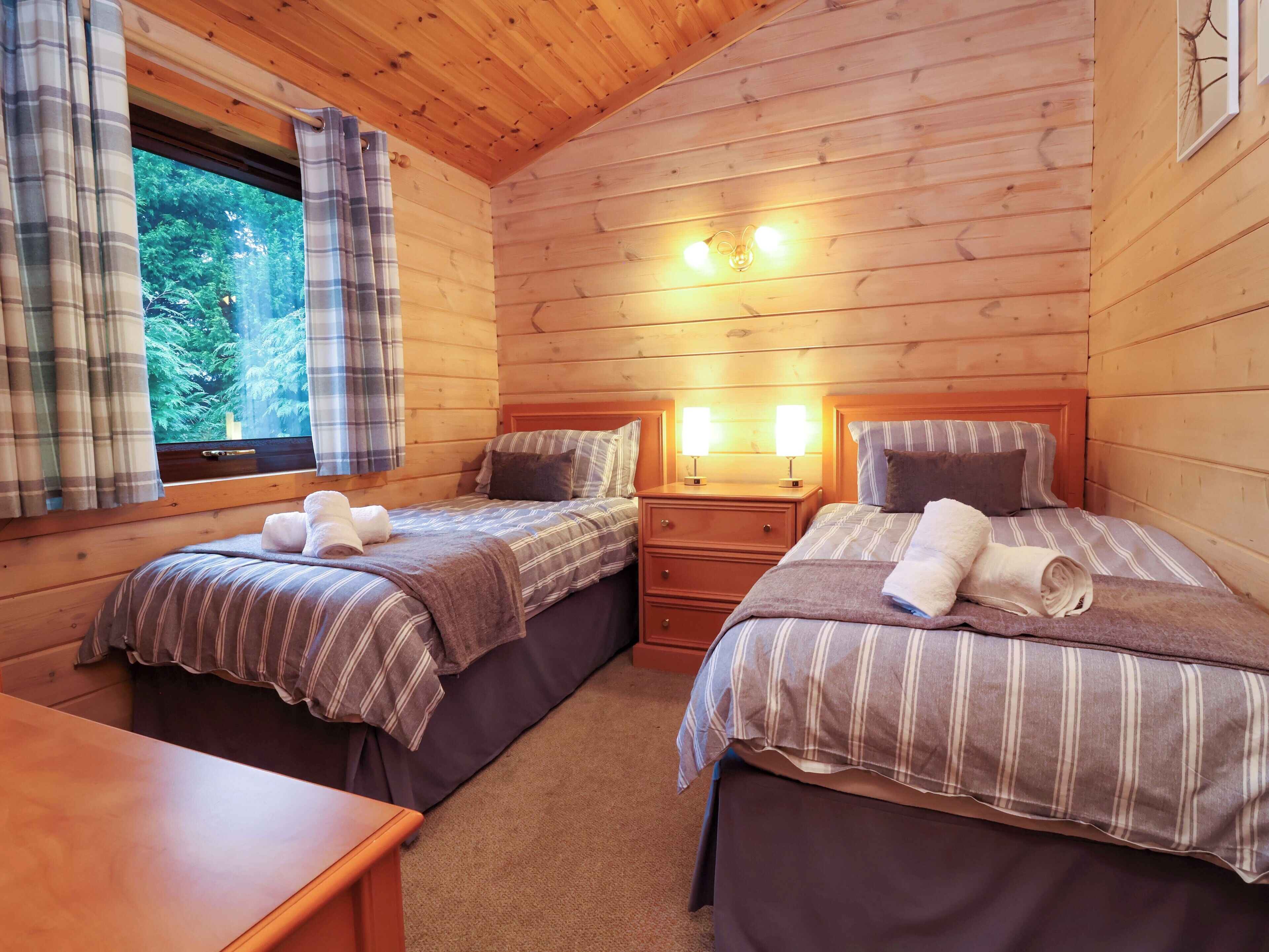 A cozy cabin room with two beds, a wooden table, and a window with curtains.