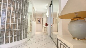 A hallway with a glass partition, a white tiled floor, and a large vase on a table. - HENRI CAMILLE AGENCY- Croisette - 2 bedrooms, 2 Bathrooms, 50m Croisette (Cannes)